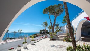 Un hôtel situé sur la côte, offrant une vue dégagée sur la mer, doté d’une promenade dallée agrémentée de jardinières et présentant un design architectural moderne.