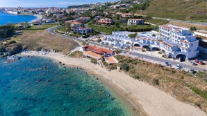Vue aérienne d’une ville côtière, avec un imposant bâtiment blanc agrémenté de touches de bleu, une plage de sable et des eaux d’un bleu limpide.