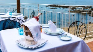 Une table dressée pour le dîner, avec vue sur la mer, une rambarde en métal et une côte rocheuse.