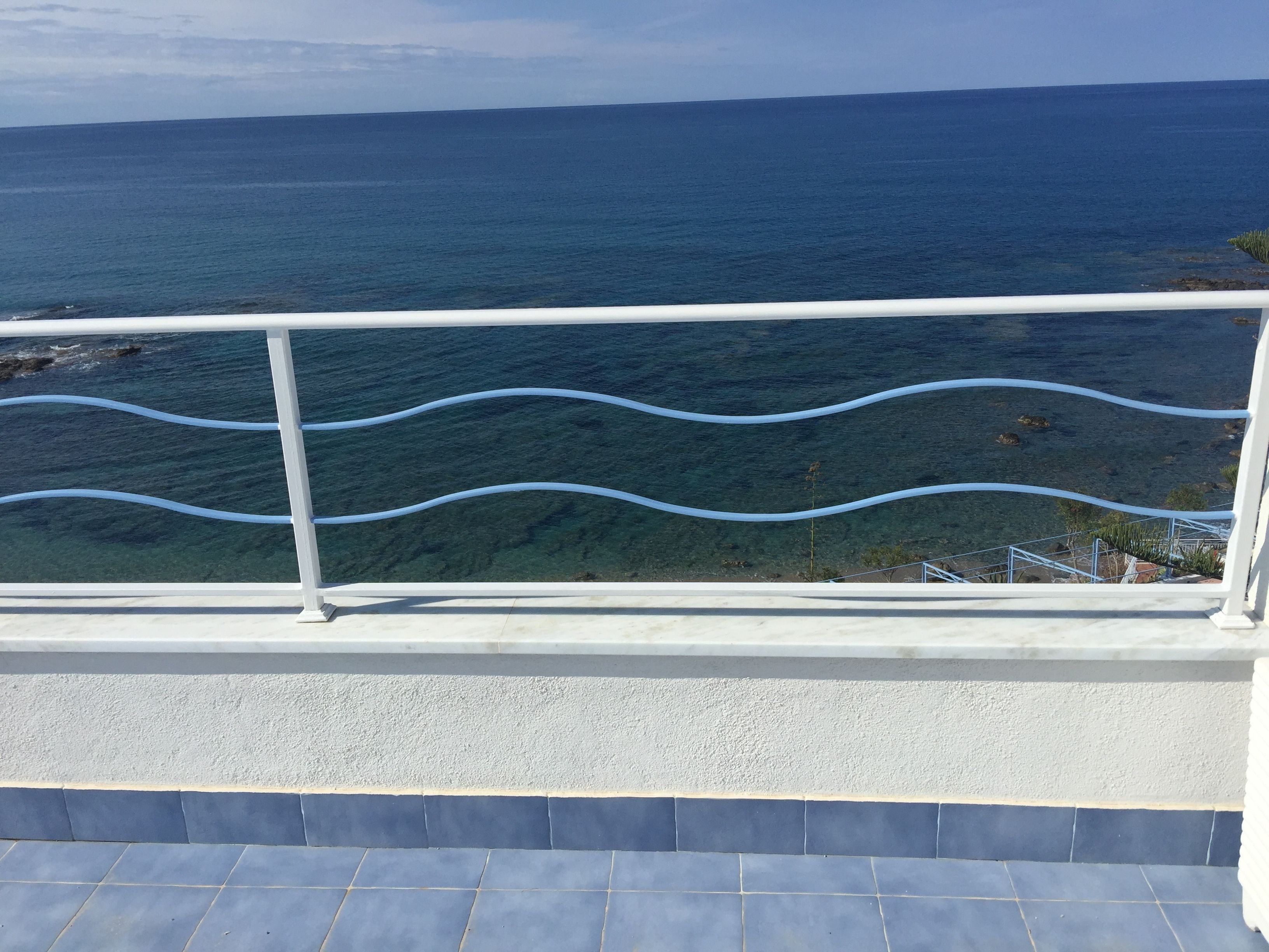 Ein Balkon mit weißer Brüstung mit Blick auf das klare, blaue Meer.