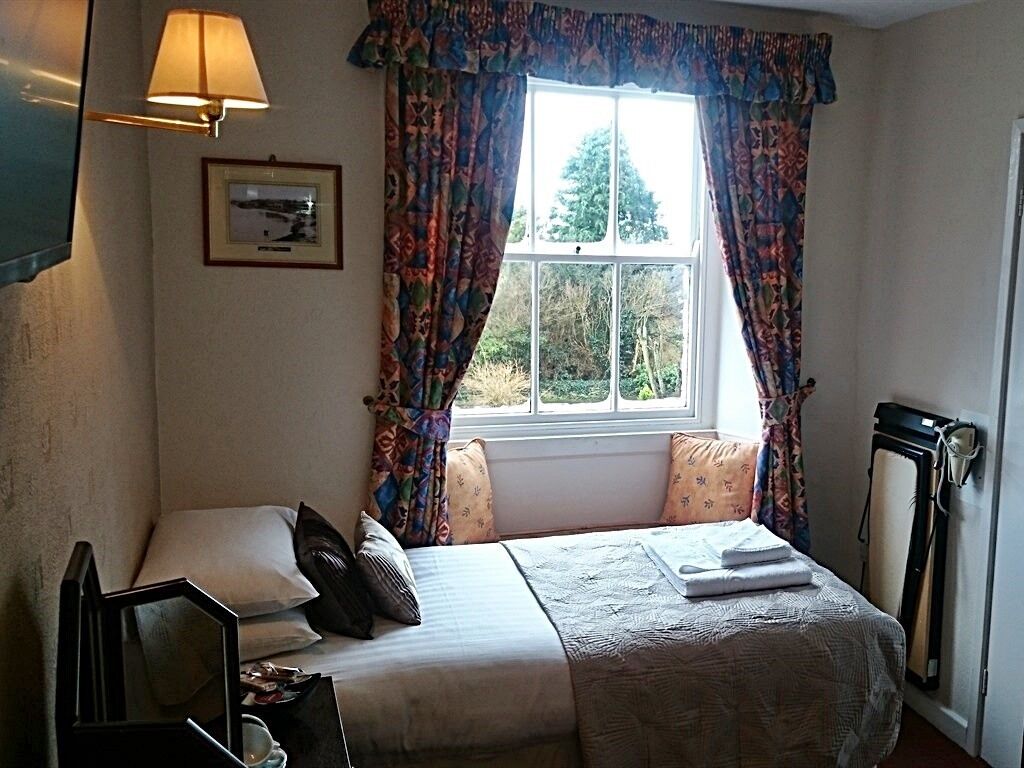 A bedroom with a bed, a bedside table, a lamp, a window with curtains, and a radiator.