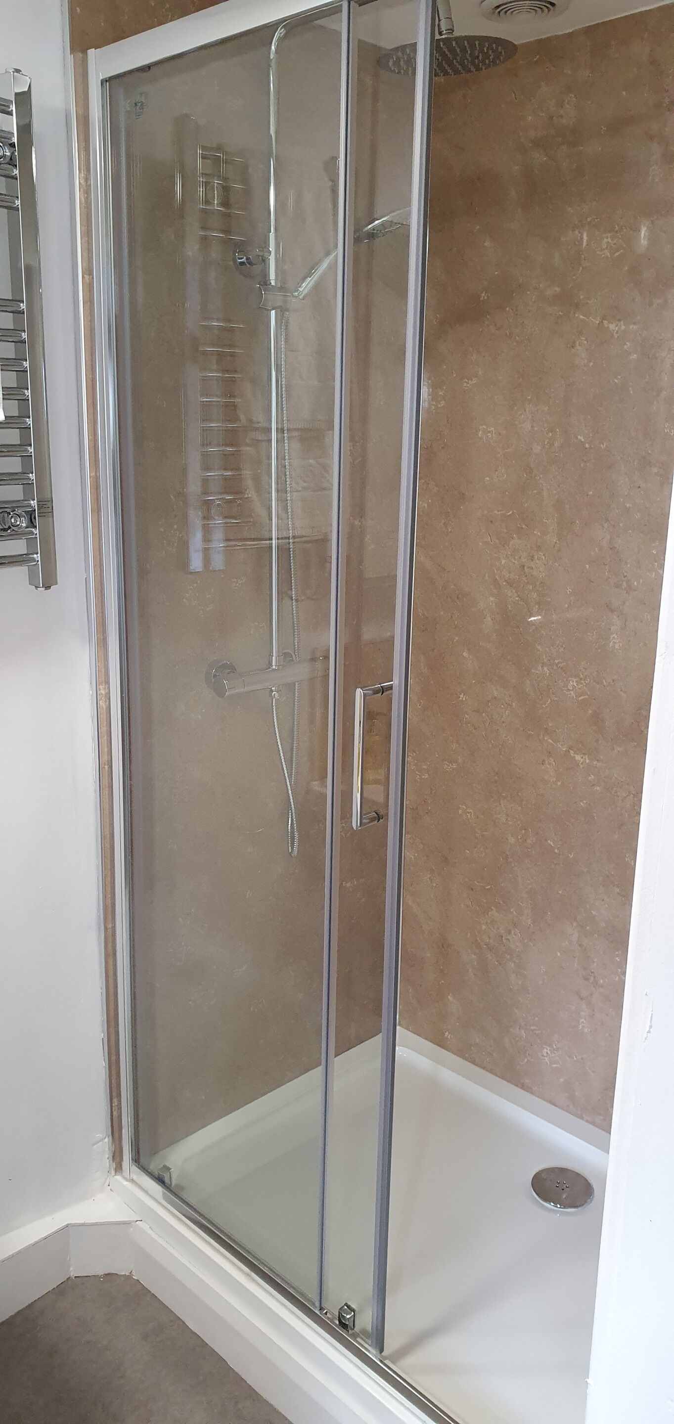 A glass-enclosed shower stall with a white floor, a metal towel rack, and a beige wall.