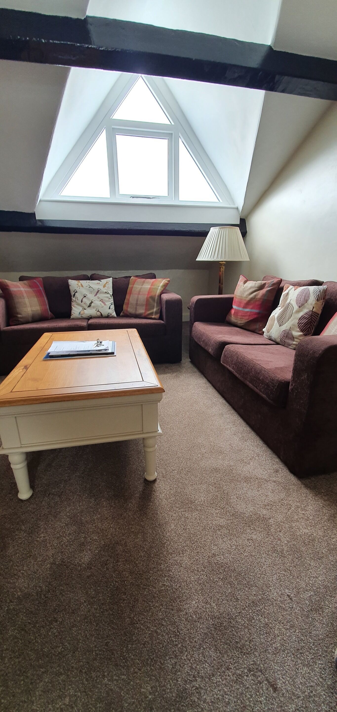 Una sala de estar acogedora con techo alto y tragaluces, amoblada con dos sofás y una mesa de centro de madera.
