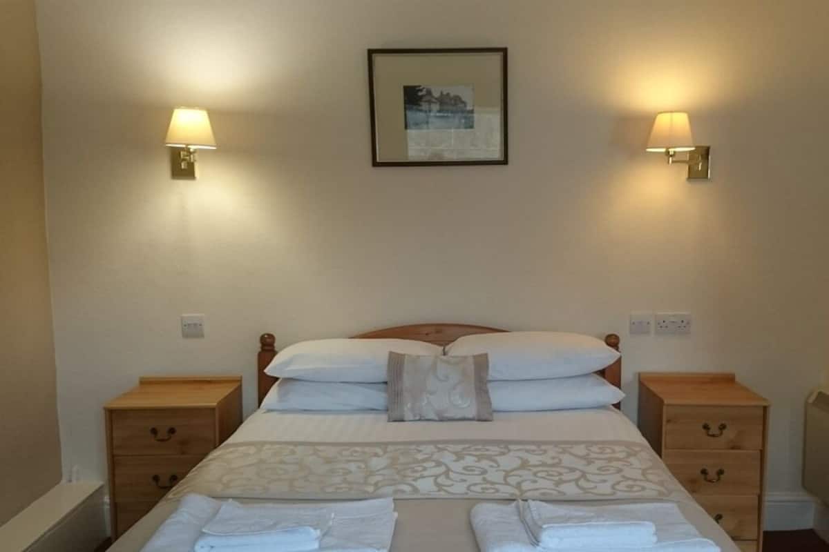 Una cama bien hecha con una colcha estampada, dos lámparas de noche y un cuadro enmarcado en la pared.