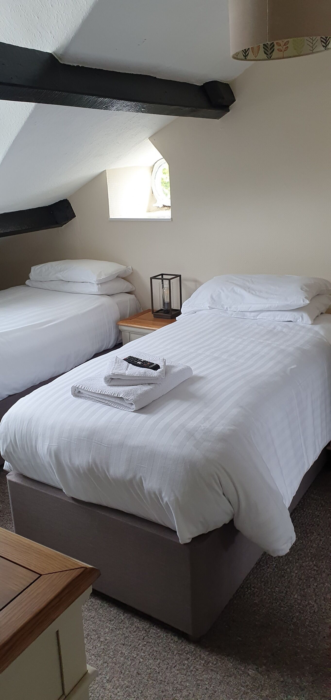 Een hotelkamer met twee bedden, een houten nachtkastje, een lamp en een raam met uitzicht.