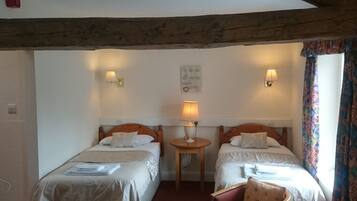 Habitación de hotel con dos camas individuales, una mesita con lámpara, una silla y una ventana con cortinas.