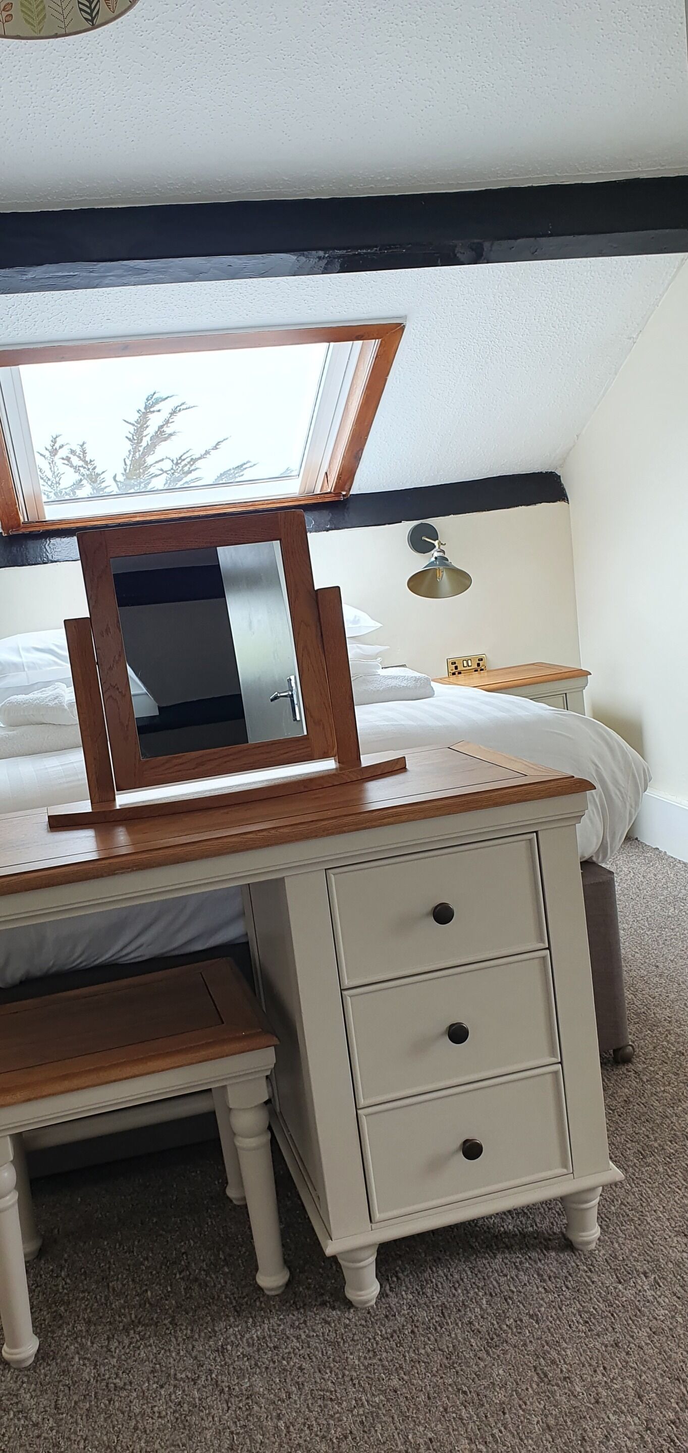 A bedroom with a bed, a wooden desk with drawers, a mirror, and a window with a view of trees.
