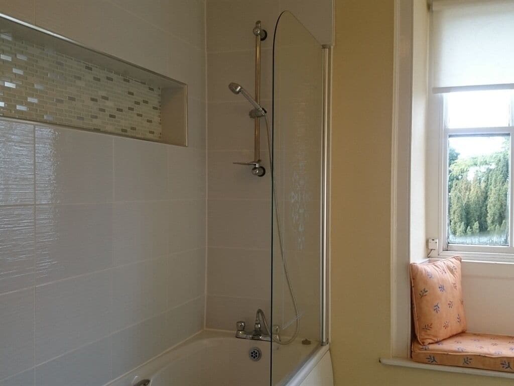 A bathroom with a glass-enclosed shower, a window with a view of trees, and a bench by the window.