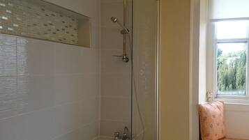 A bathroom with a glass-enclosed shower, a window with a view of trees, and a bench by the window.