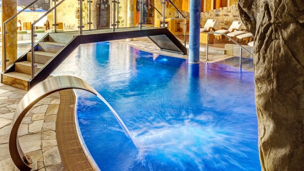 Una piscina interior con suelo de piedra, una escalera que lleva a un balcón y un mural en el techo.