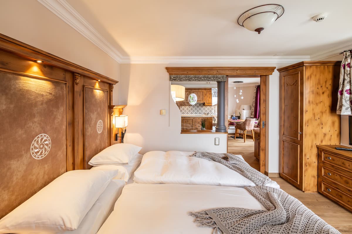 A hotel room with a large bed, wooden headboard, and a view into the kitchen area.