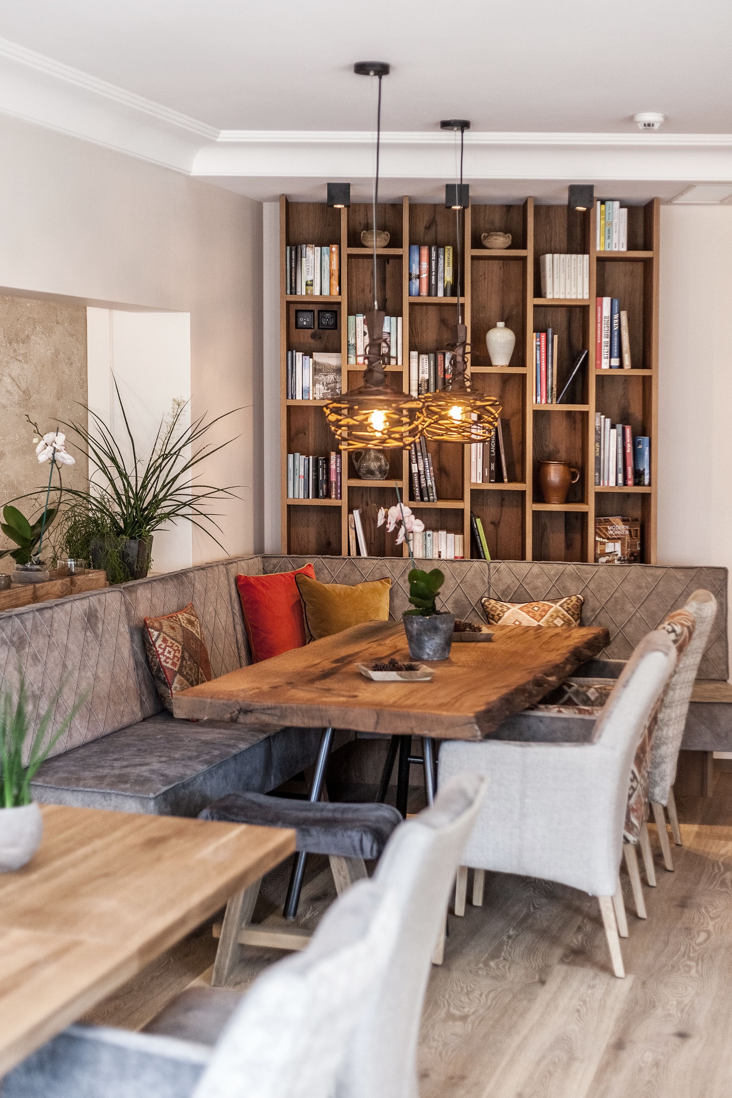 Een moderne woonkamer met een houten eettafel, zachte zithoek en een grote boekenkast vol boeken en decoratieve objecten.