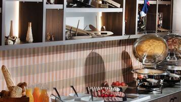 A breakfast buffet with various food items, a coffee machine, and kitchen utensils on shelves.