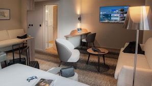 Una habitación de hotel con cama, escritorio, silla, sofá y televisor en la pared.