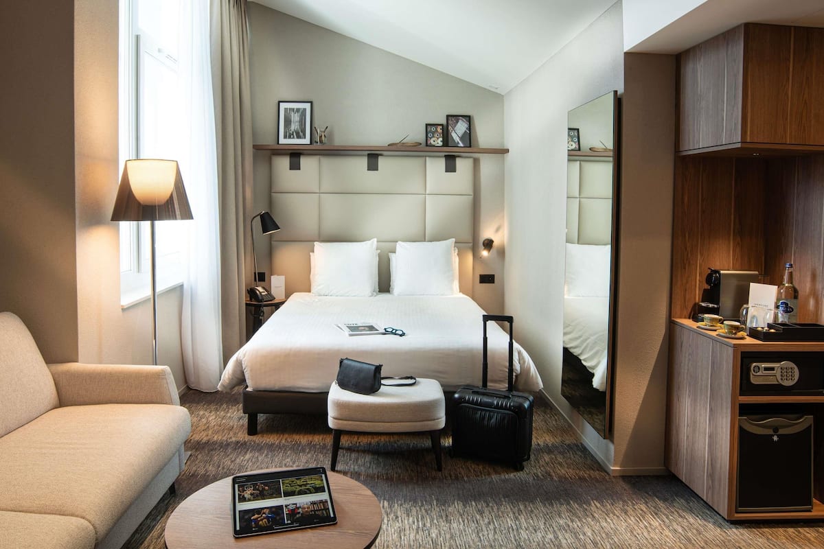 Une chambre d’hôtel avec un grand lit, un bureau, une chaise, une petite table et un mini-bar.