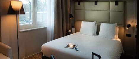 A hotel room with a large bed, a bedside table, a lamp, a chair, and a suitcase.