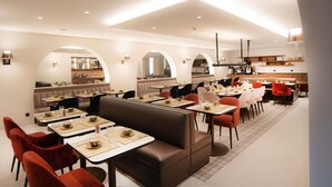 Un restaurante moderno con cabinas y mesas, una cocina al fondo y un diseño limpio y contemporáneo.