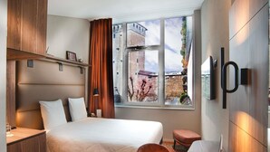 A hotel room with a bed, desk, laptop, and a view of a building through the window. - Mercure Fribourg Centre Remparts (Fribourg)