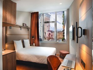 Una habitación de hotel moderna con una cama, escritorio, ordenador portátil y un ventanal con vistas a la ciudad.