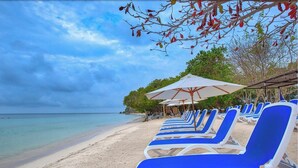 A beach with rows of blue and white sun loungers, a white umbrella, and a clear view of the ocean. - Hotel Isla del Encanto (Cartagena)