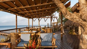 An outdoor wooden deck with wicker furniture, a thatched-roof structure, and a view of the sea. - Hotel Isla del Encanto (Cartagena)