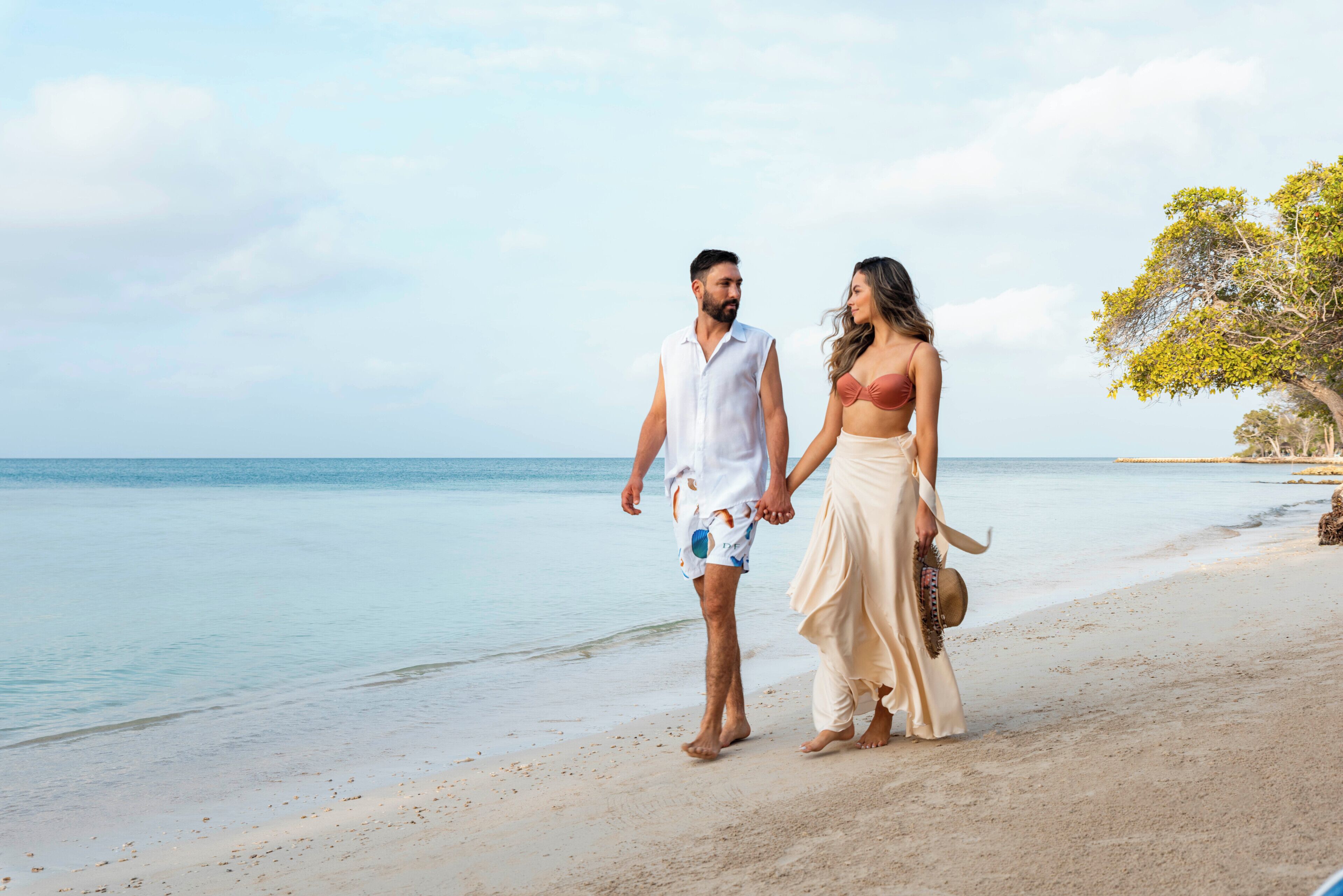 A couple walking on a beach with a clear sky and calm sea.