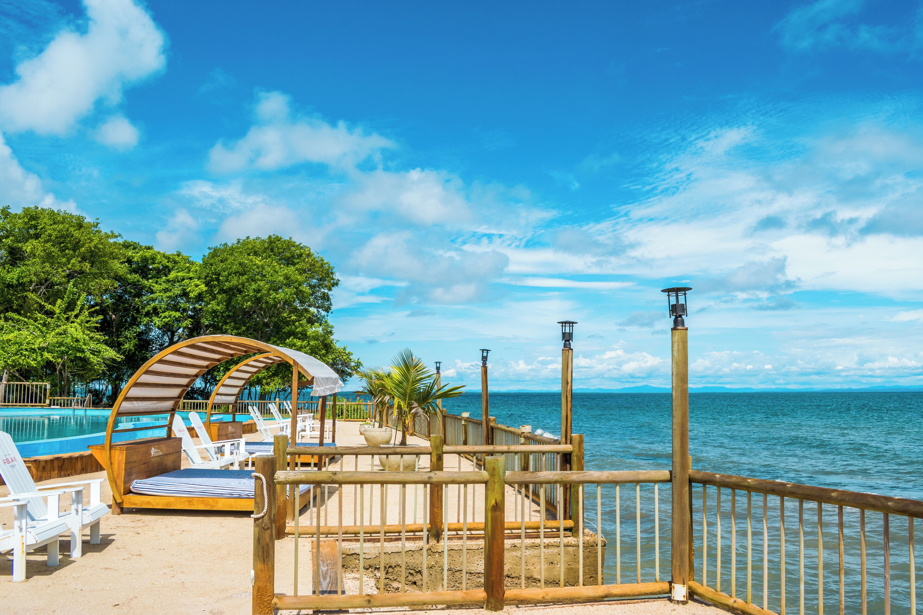 A beachside pool area with lounge chairs, a wooden deck, and a view of the ocean.