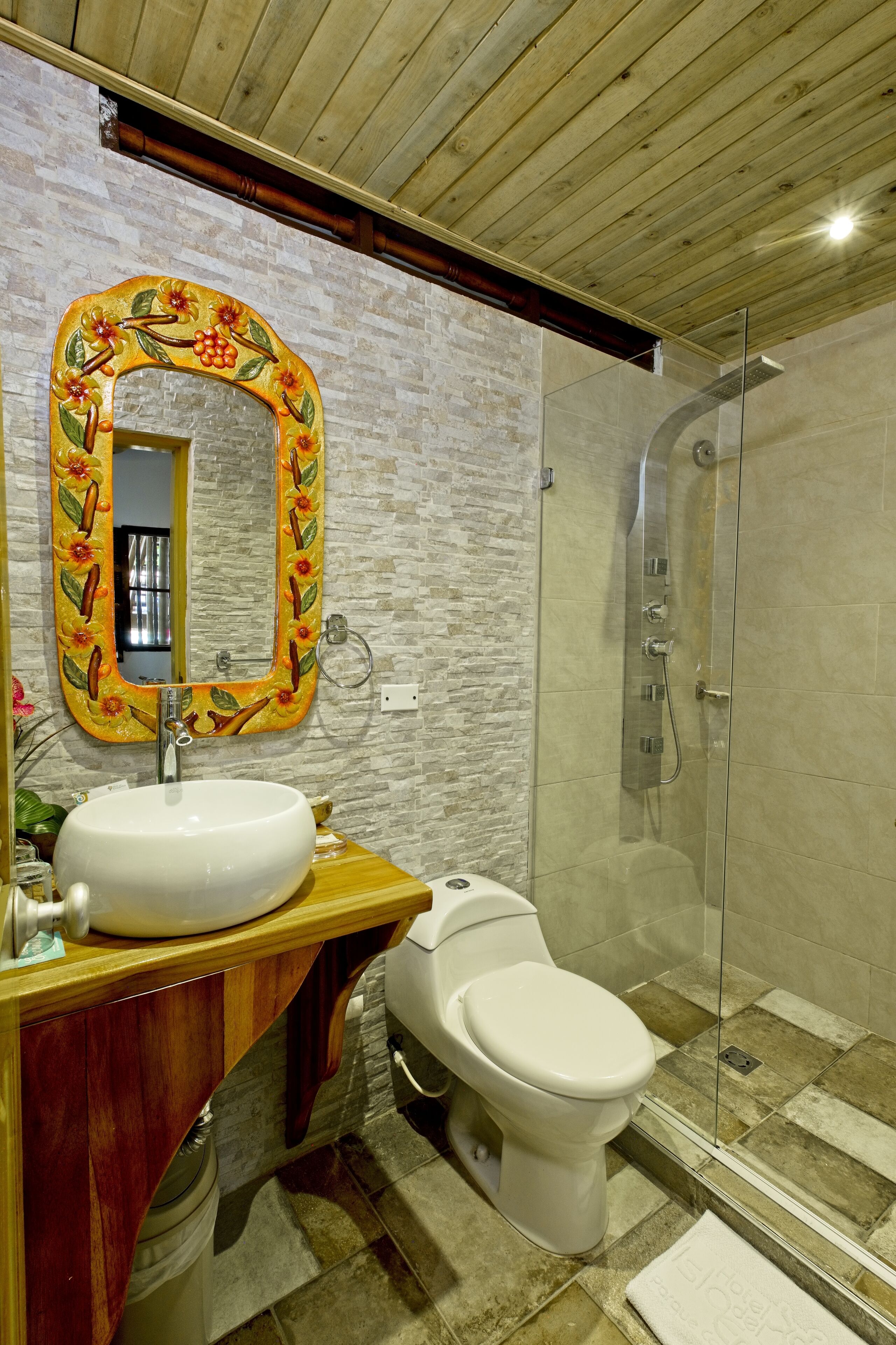 Un baño con tocador de madera, un lavabo blanco, un inodoro y una ducha con mampara de vidrio.