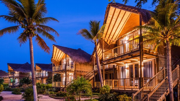 A resort with multiple wooden buildings, each with a thatched roof and a balcony. There are palm trees and a well-maintained garden in front of the buildings. - Hotel Isla del Encanto (Cartagena)
