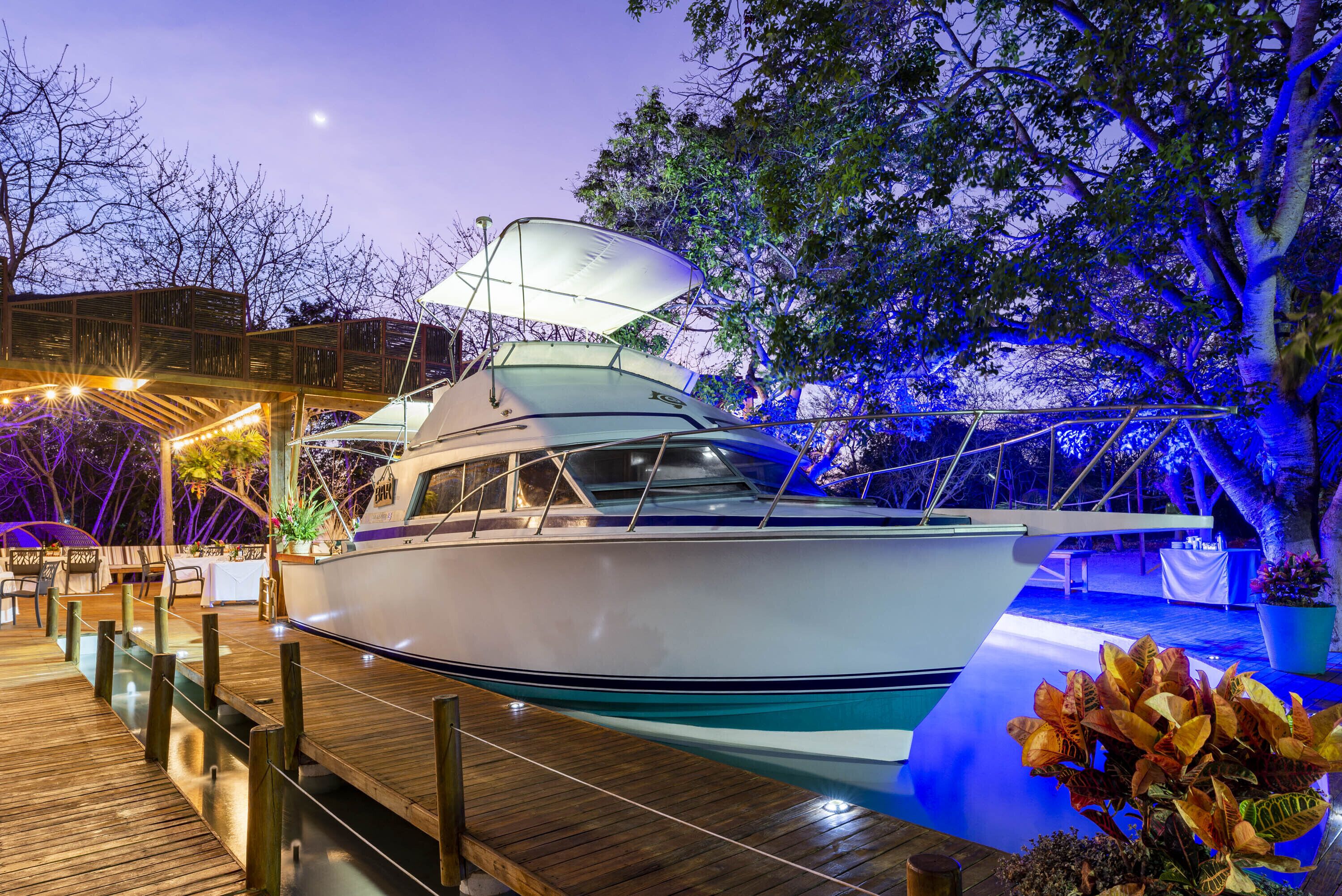 A white yacht docked at a wooden pier with a covered seating area and tables.