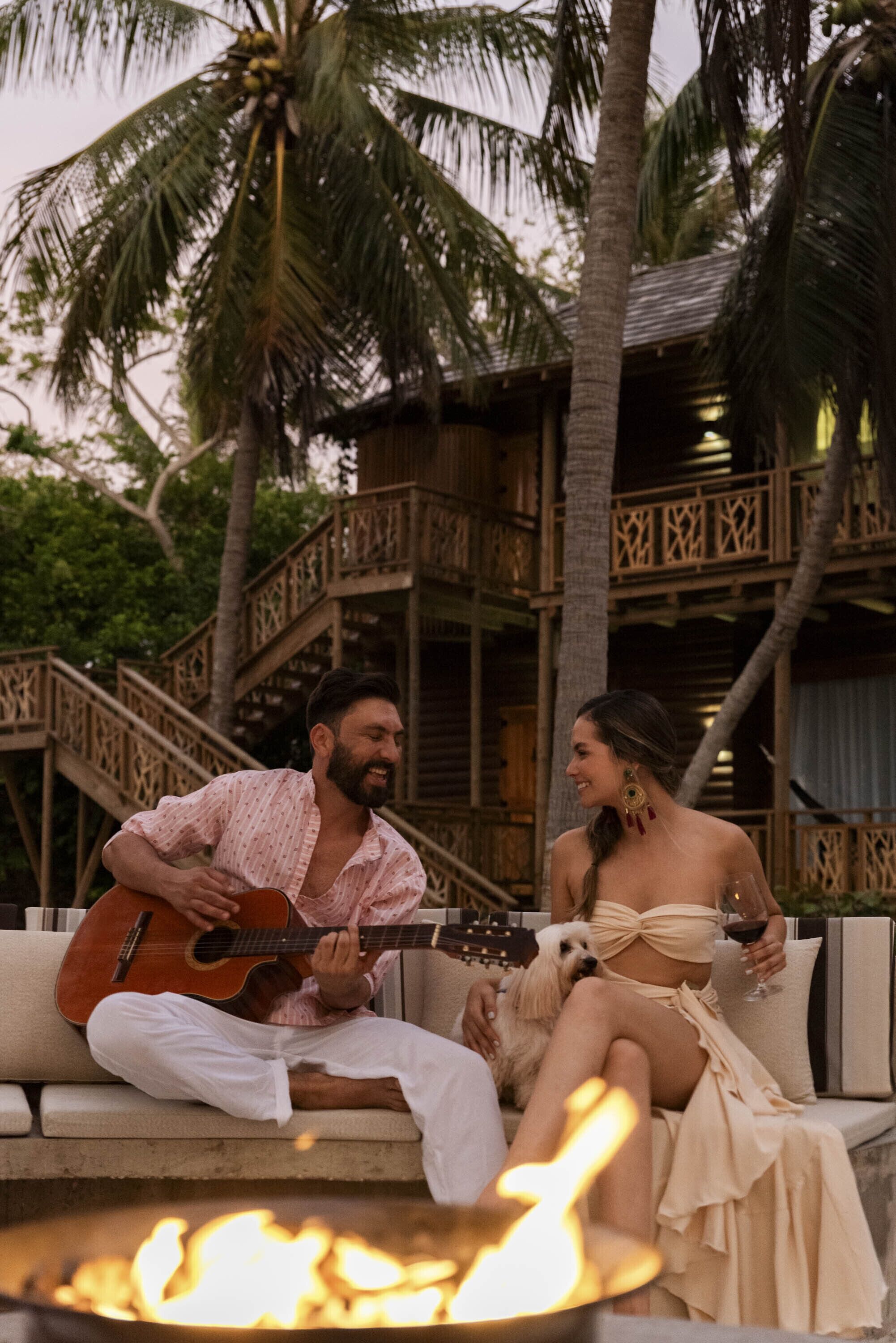 A man playing guitar on a wooden deck with a woman and a dog nearby.