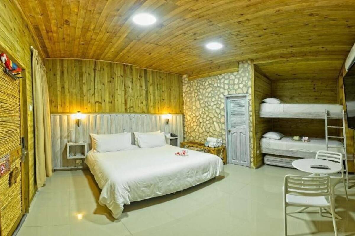 A wooden-paneled room with a bed, a stone wall, a television, and a bunk bed.