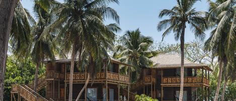 A wooden two-story building with balconies, surrounded by palm trees.