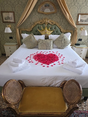 A luxurious bedroom with a bed adorned with rose petals, a golden crown headboard, and a pair of ornate chairs.
