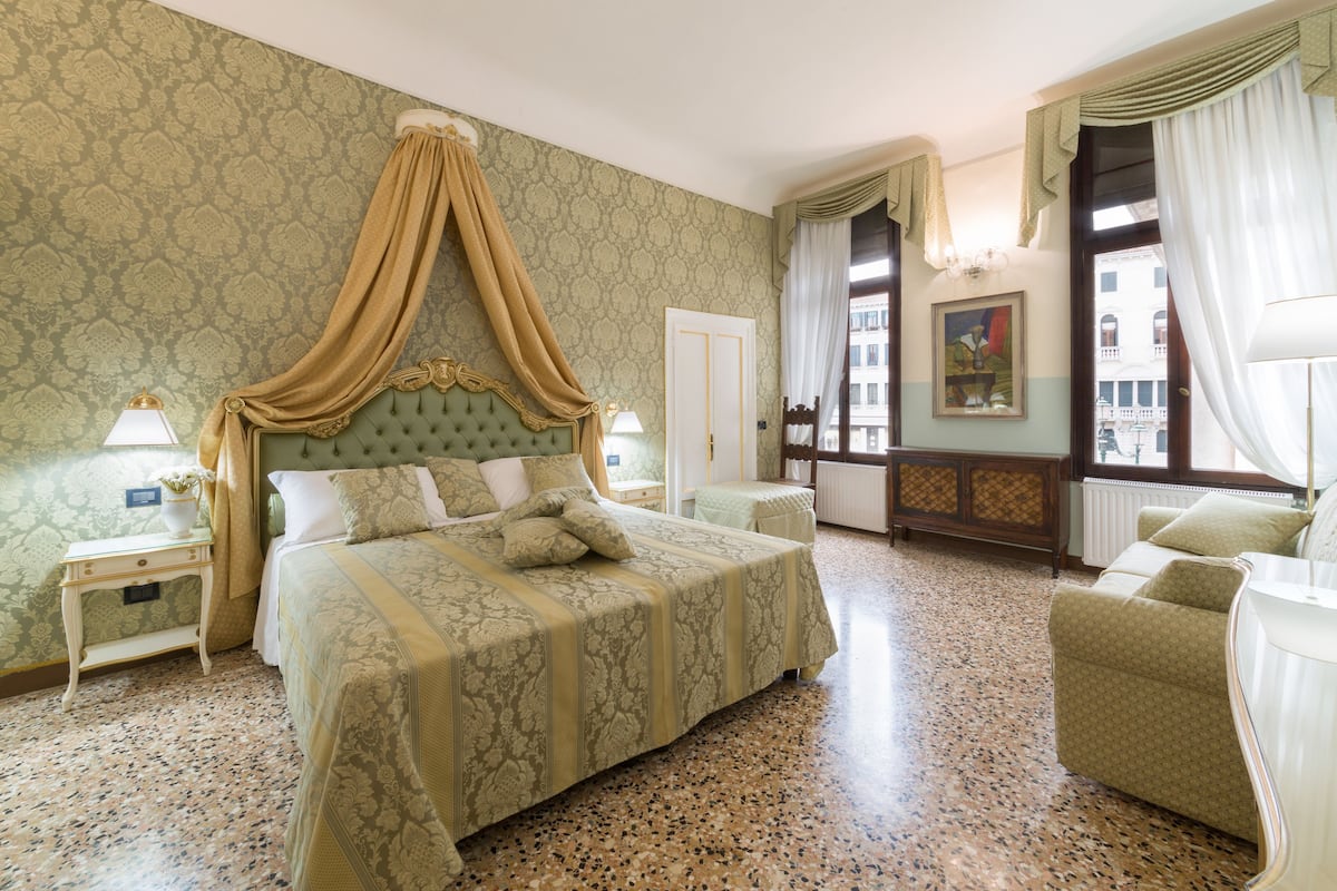 A spacious bedroom with a large bed, a nightstand, a chair, and a view of the city through the window.