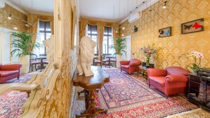 A room with a patterned carpet, red chairs, a white statue, and a large window.