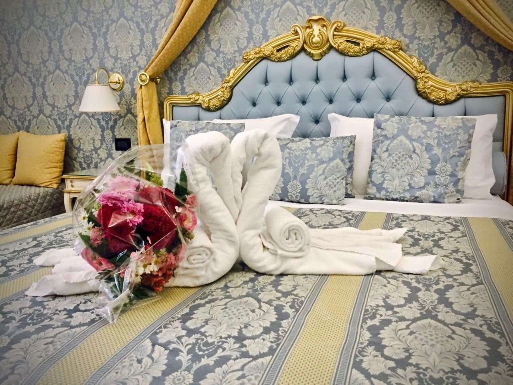 Um quarto luxuoso com cabeceira estofada, espaldar com padrão floral e um buquê de flores.