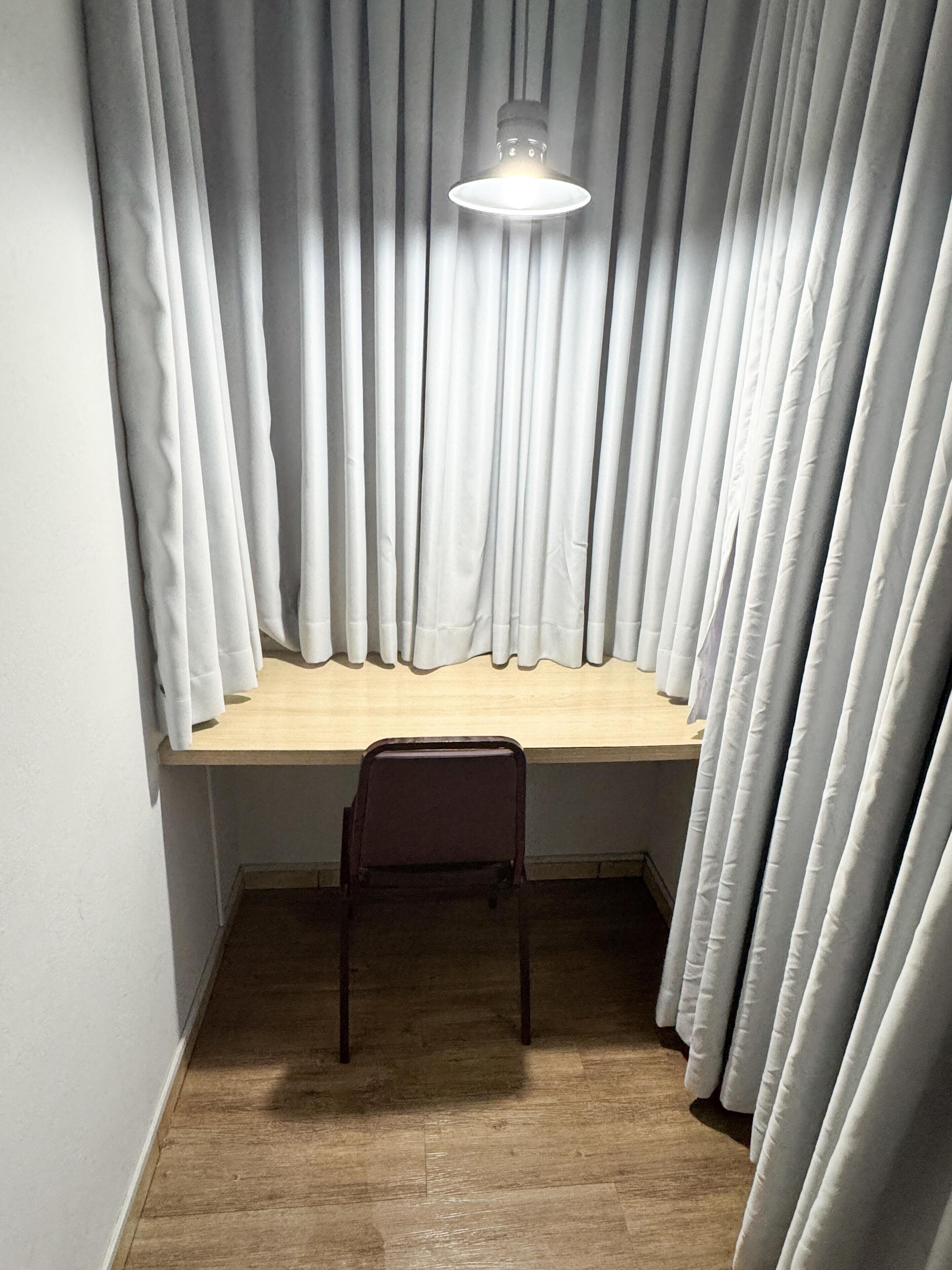 Una habitación con un escritorio de madera, una silla y una lámpara colgante.