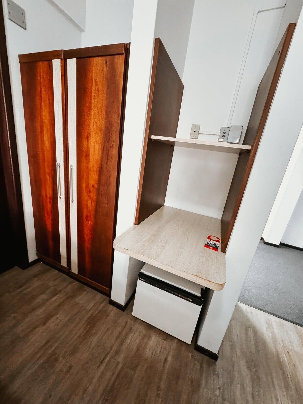 A room with a wooden wardrobe, a white desk with a shelf, and a white cabinet.