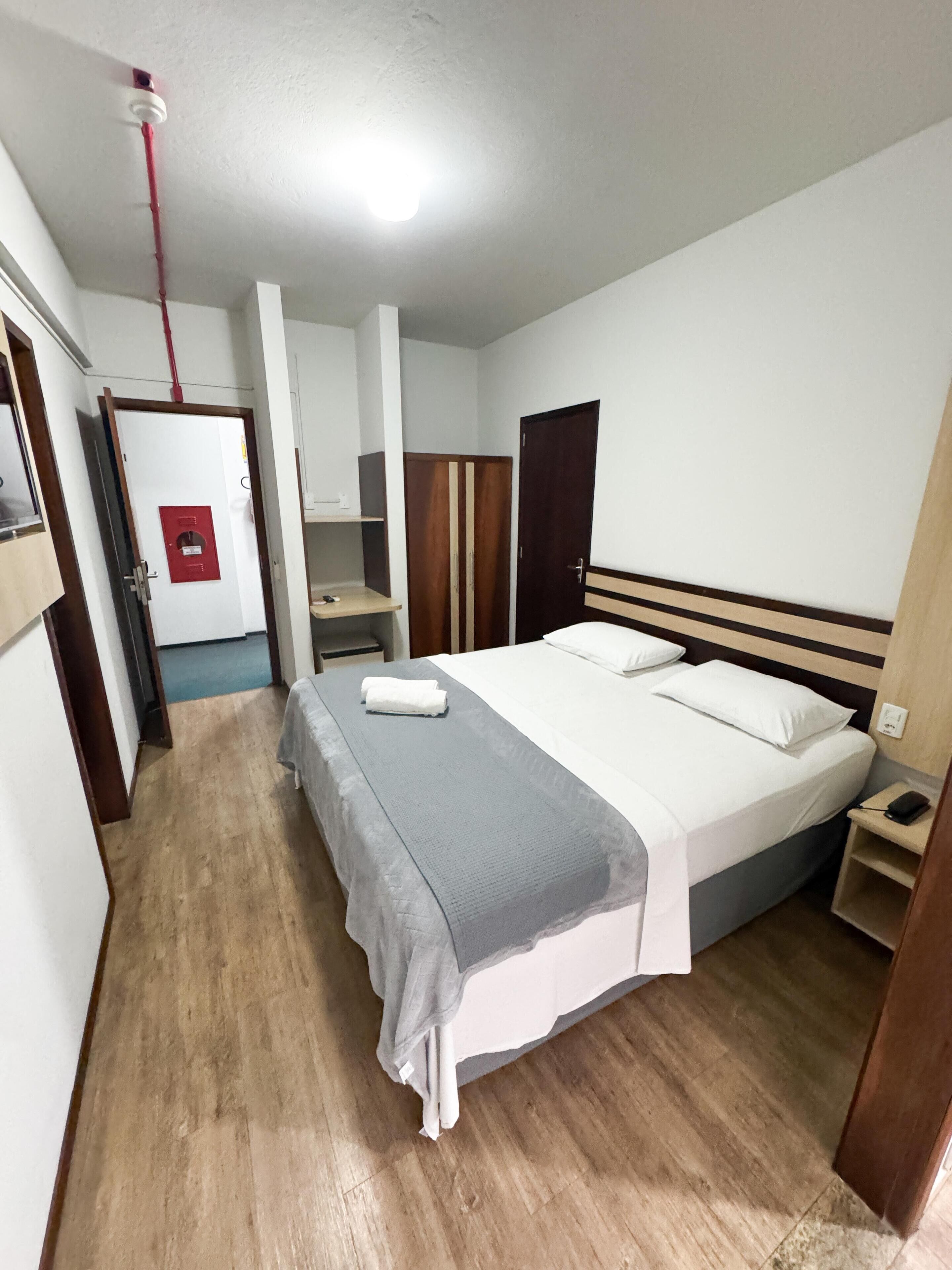 Habitación de hotel con cama, mesita de noche, armario y un letrero de salida de emergencia rojo.