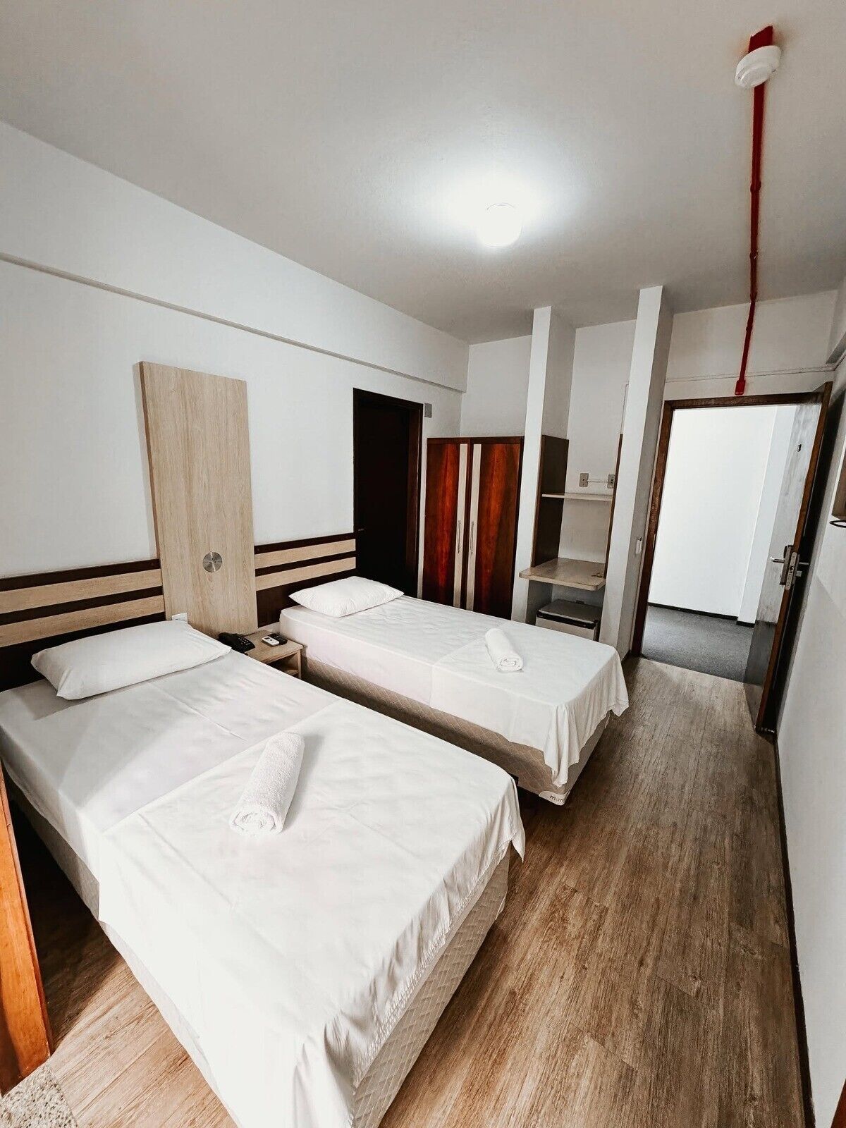 Una habitación de hotel con dos camas individuales, un armario de madera, un escritorio y un espejo.