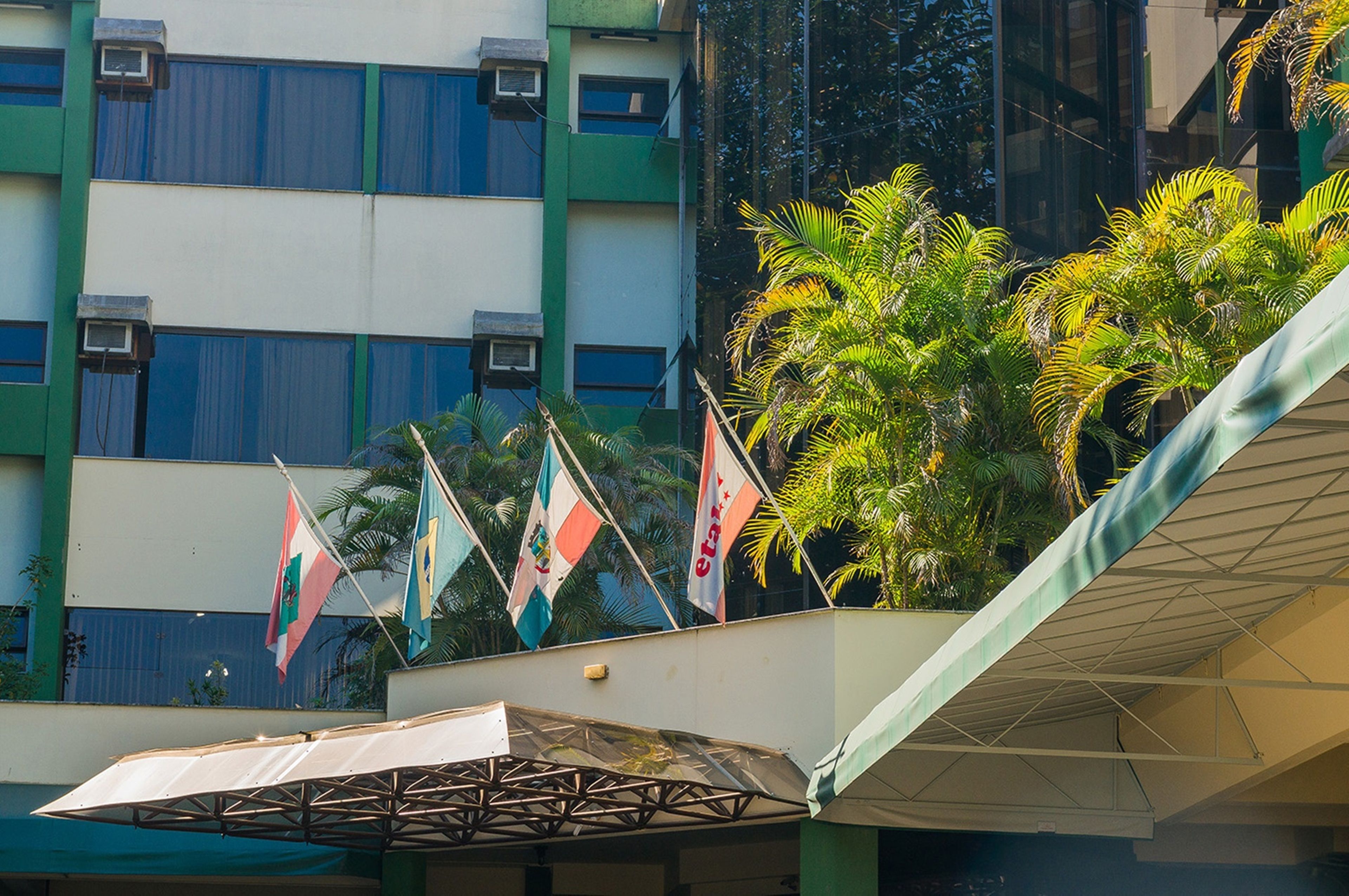 A building with multiple flags, a covered outdoor area, and palm trees.