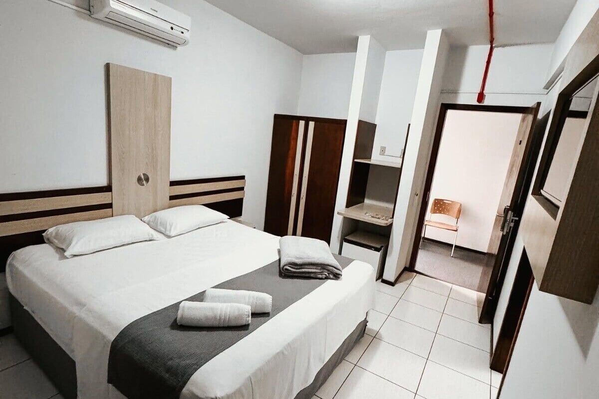 A modern hotel room with a large bed, a wardrobe, a TV, and a bathroom visible through an open door.