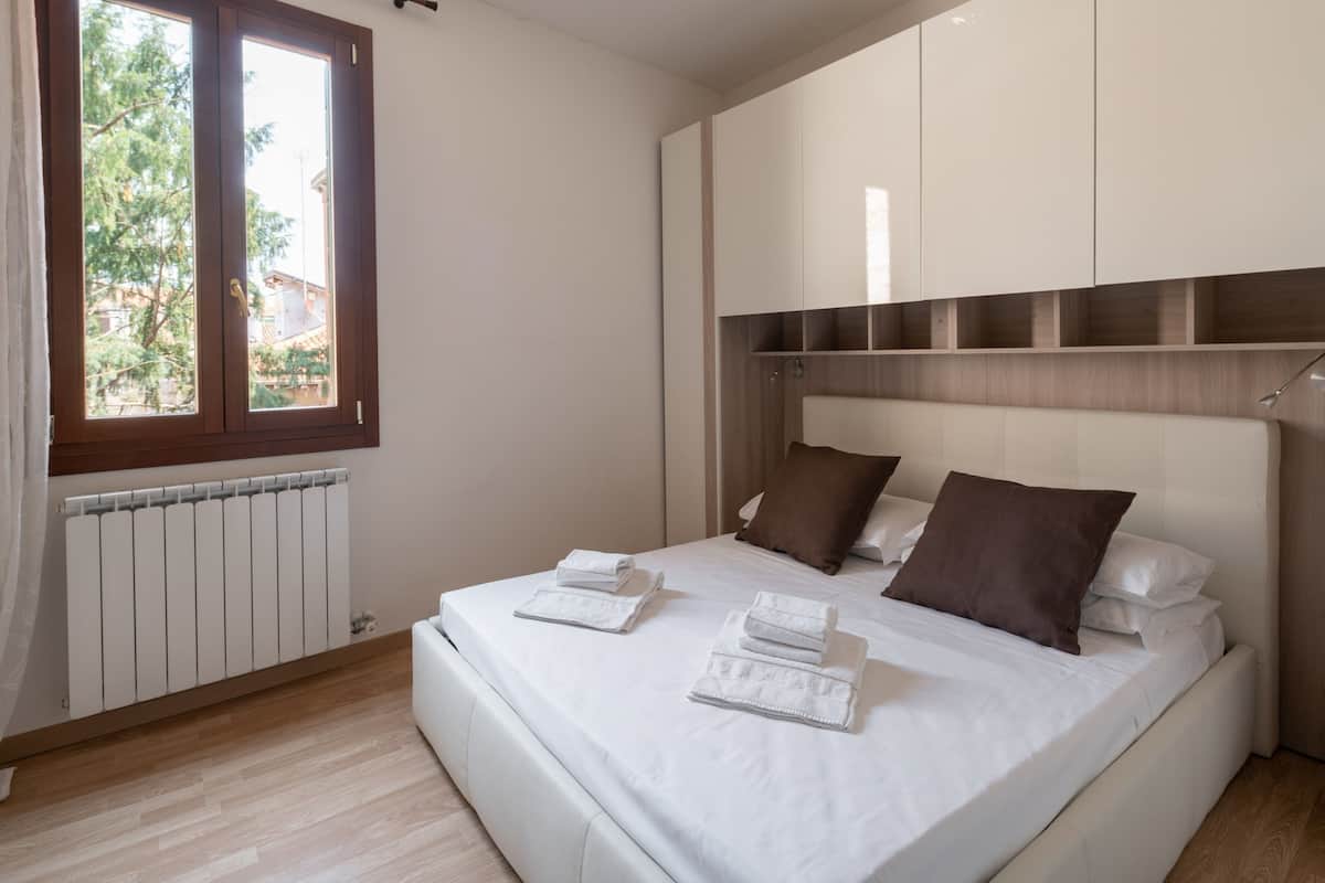 A bedroom with a large bed, white linens, brown pillows, and a window with curtains.
