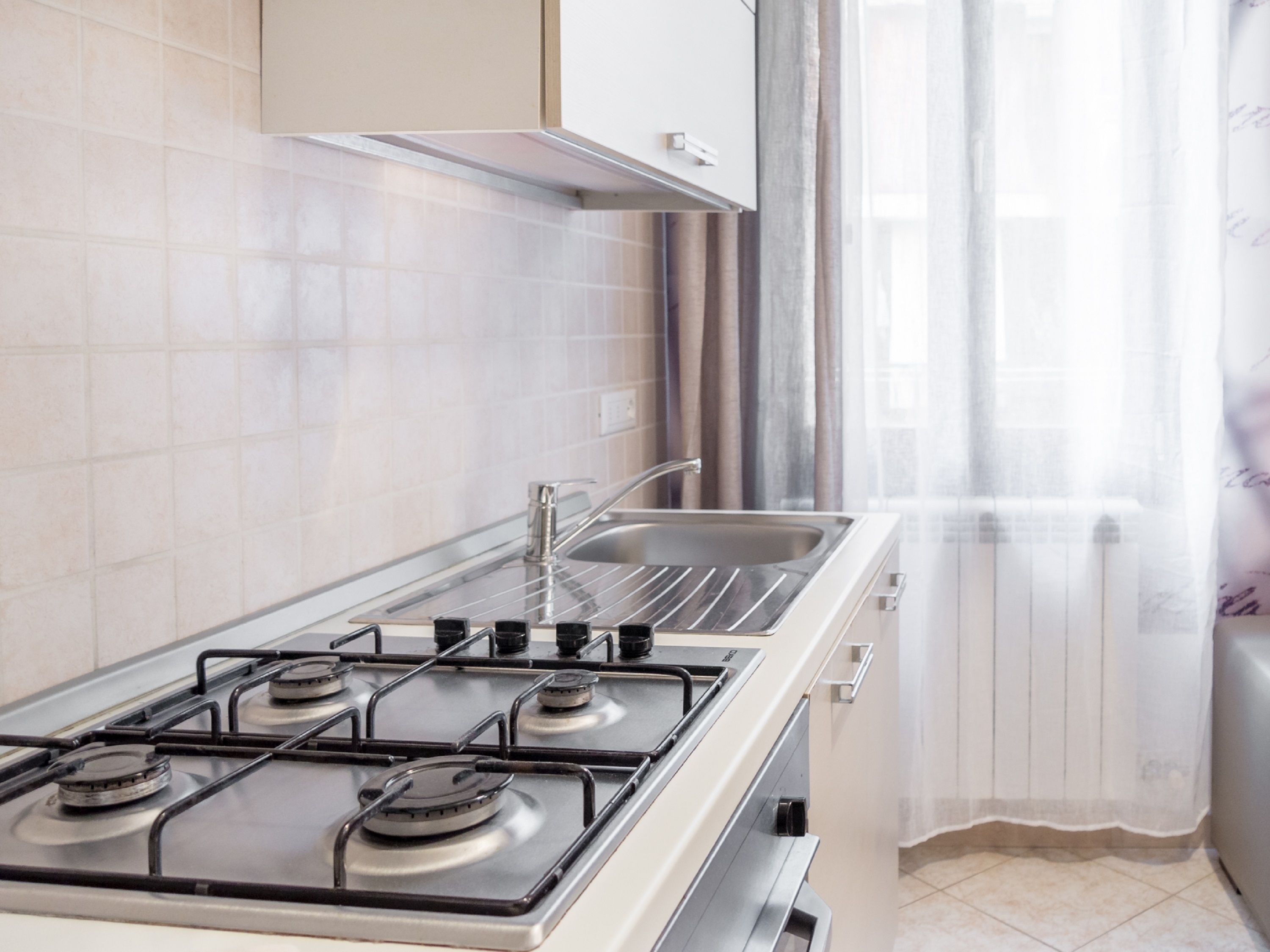 Una cocina con estufa a gas, un lavabo y una ventana con cortinas.