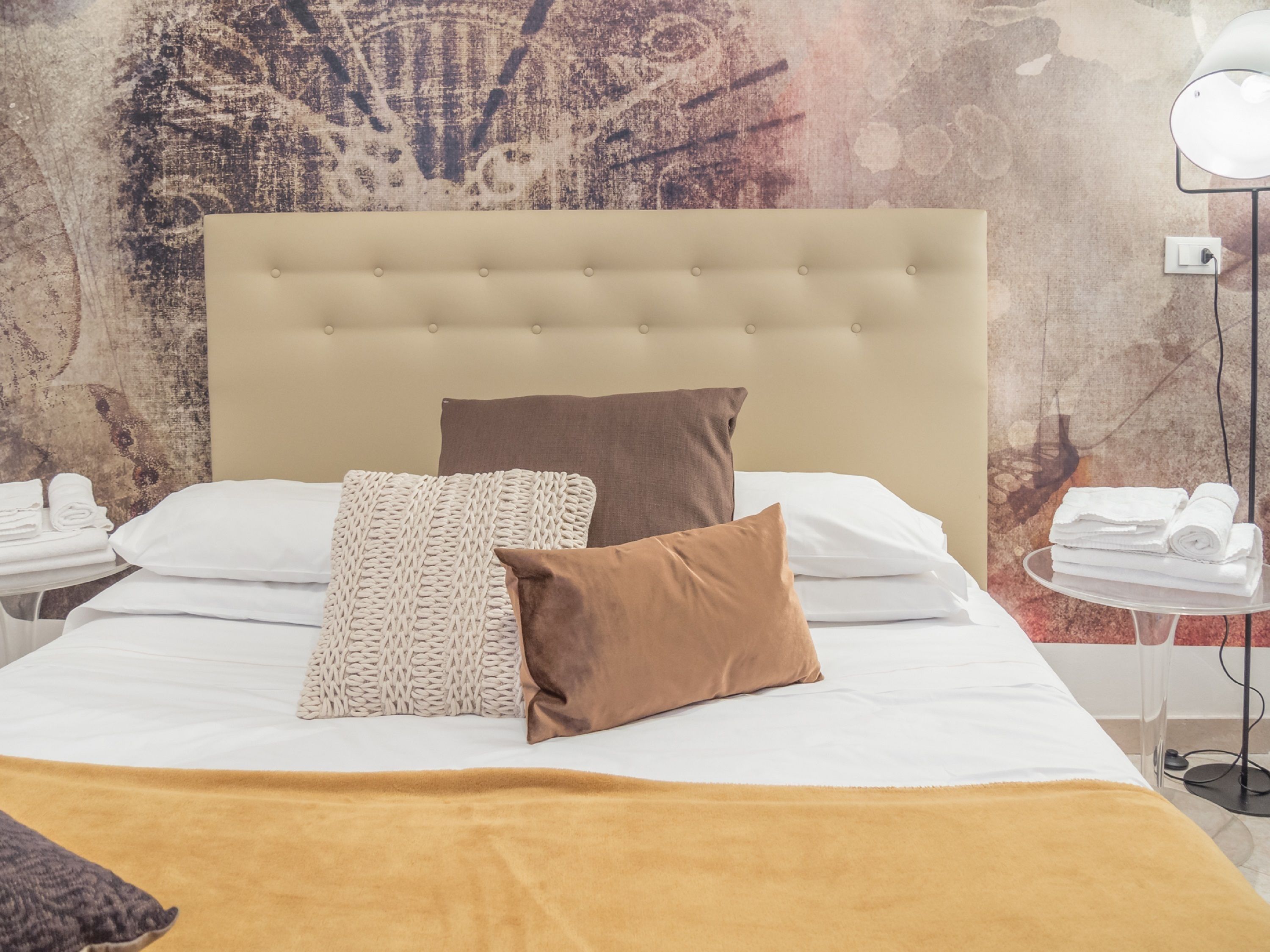 A neatly made bed with a beige headboard, white and brown pillows, and a yellow throw blanket.