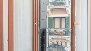 A room with a bed, a window with a view of a balcony, and a door. - San Polo Canal View Apartments by Wonderful Italy (Venice)