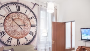 A living room with a large decorative clock, a sofa with cushions, a television, and a wooden cabinet. - San Polo Canal View Apartments by Wonderful Italy (Venice)