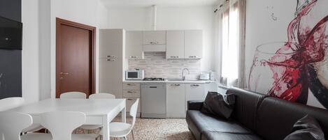 A compact living space with a kitchenette, a dining area with chairs, a sofa, and a large abstract painting on the wall.