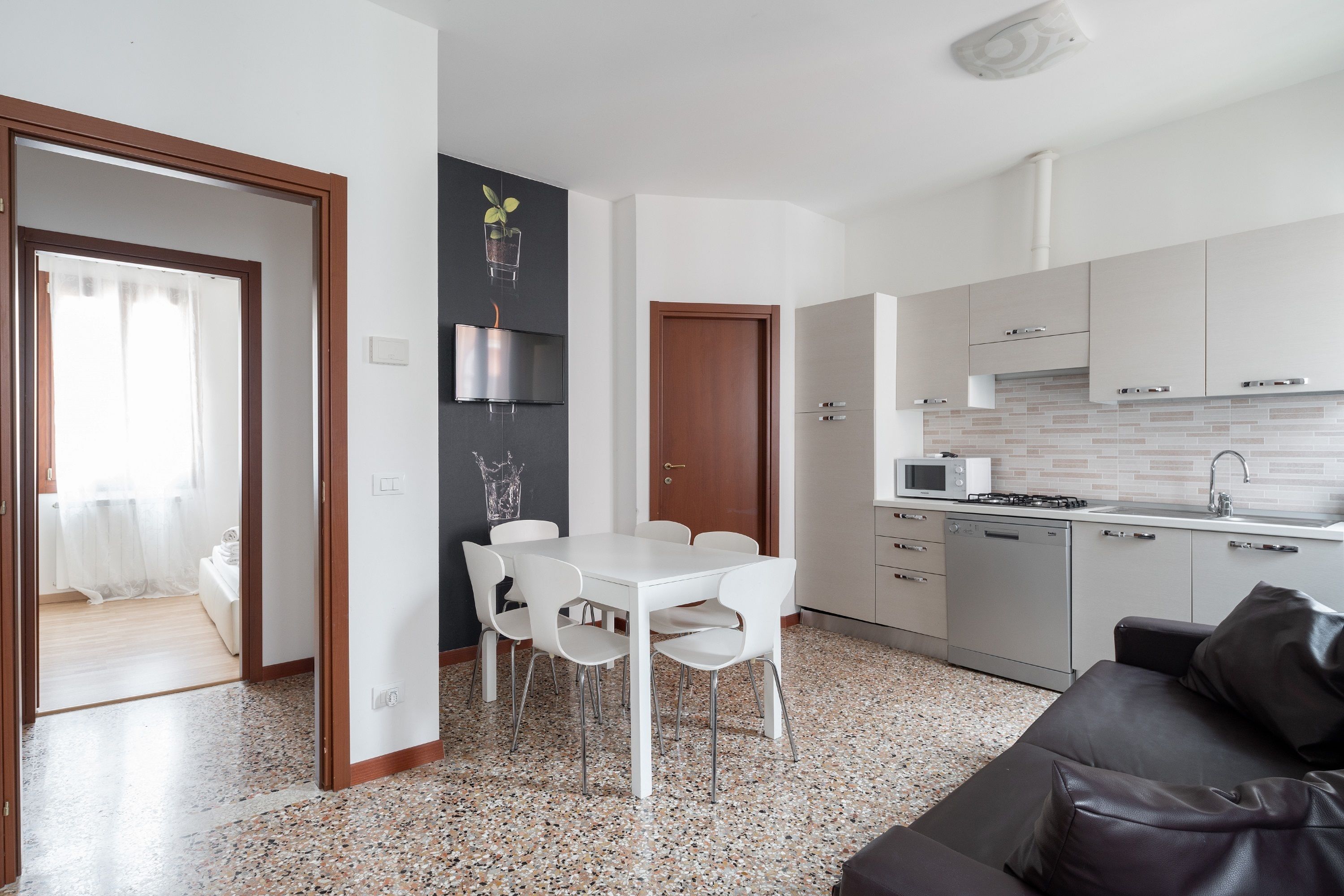A modern kitchen with white cabinets, a microwave, and a sink. There is a dining area with a white table and chairs.